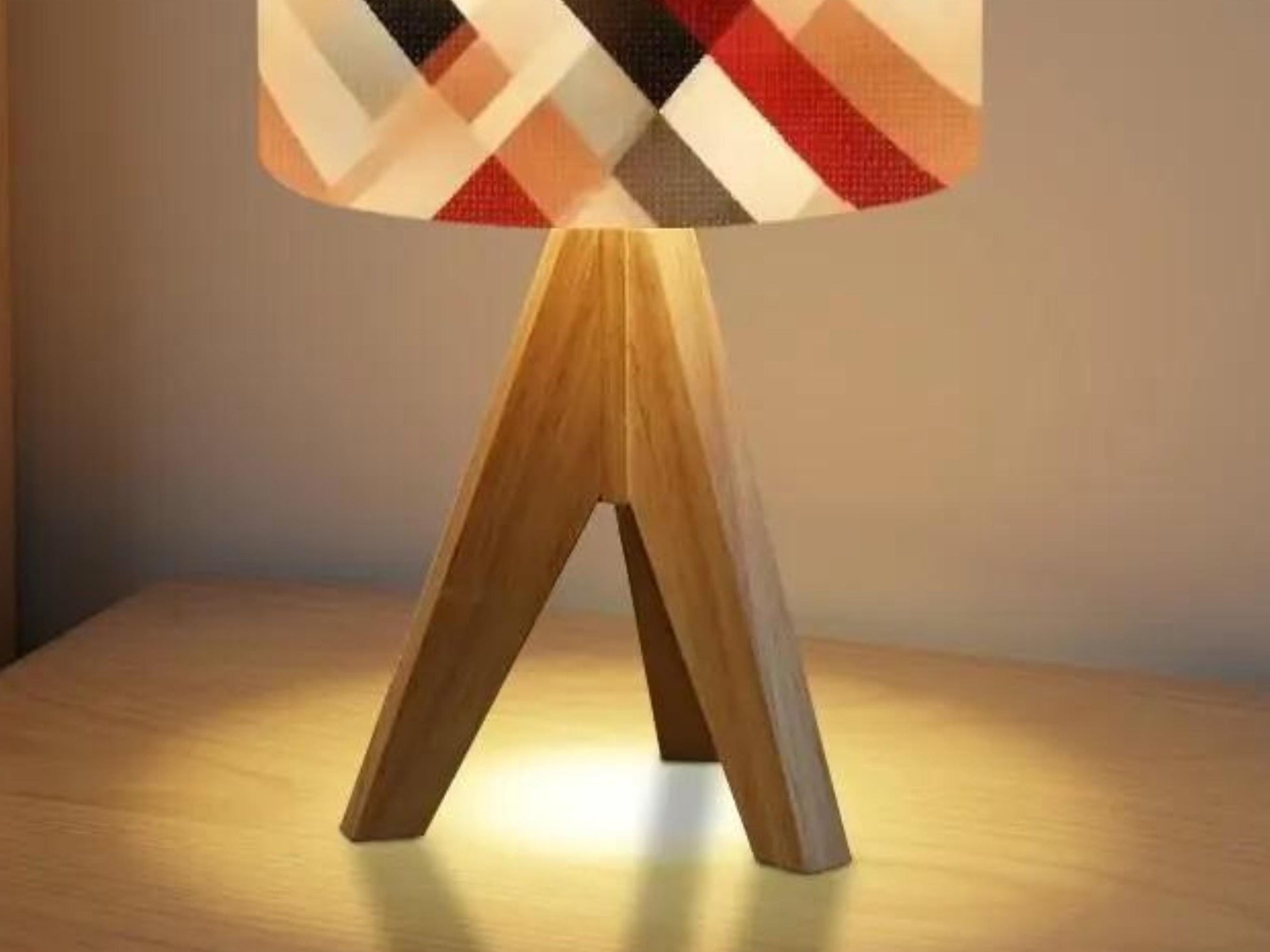 A wooden lamp base with a geometric patterned lamp shade is placed on a wooden table, casting a warm glow.