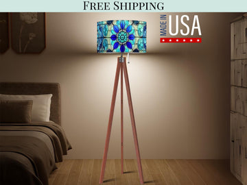 a modern bedroom with a wooden tripod floor lamp featuring a colorful stained glass design. The lamp is placed on a wooden stand, and the text "FREE SHIPPING MADE IN USA" is displayed above it.