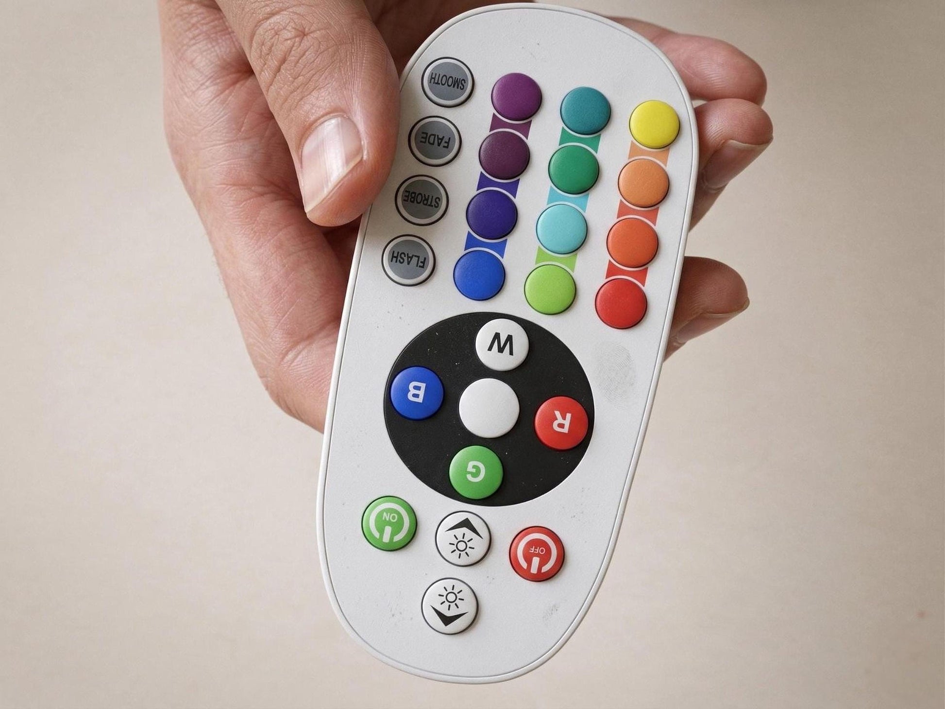 A hand is holding a remote control with a variety of colorful buttons, including a central button with a white circle and a black "M" in the center.