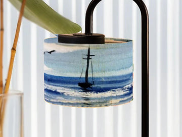 a lamp shade with a painting of a sailboat on the ocean.